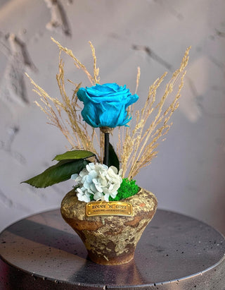 Bleu Éternelle Bloom featuring a preserved blue rose with dried botanicals in a rustic decorative pot.